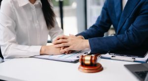 A judge's gavel sits beside the scales of justice, as an Asian business professional and a lawyer or counselor engage in a consultation.