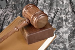Military law concept: A soldier in uniform stands beside a wooden gavel in a courtroom setting, symbolizing the intersection of military service and legal proceedings.