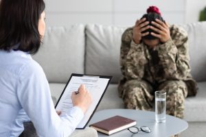 A female psychotherapist conducting a psychology survey with a depressed Black female soldier in uniform, holding a clipboard and filling out a questionnaire.