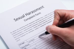 A close-up of a human hand using a pen to fill out a sexual harassment complaint form.