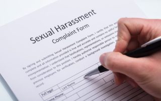 A close-up of a human hand using a pen to fill out a sexual harassment complaint form.