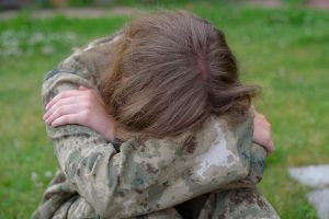 A teenage girl in camouflage, looking saddened.