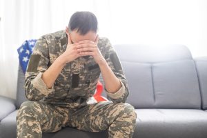 A sad soldier in a camouflage uniform holding a military tag tightly in clenched hands.